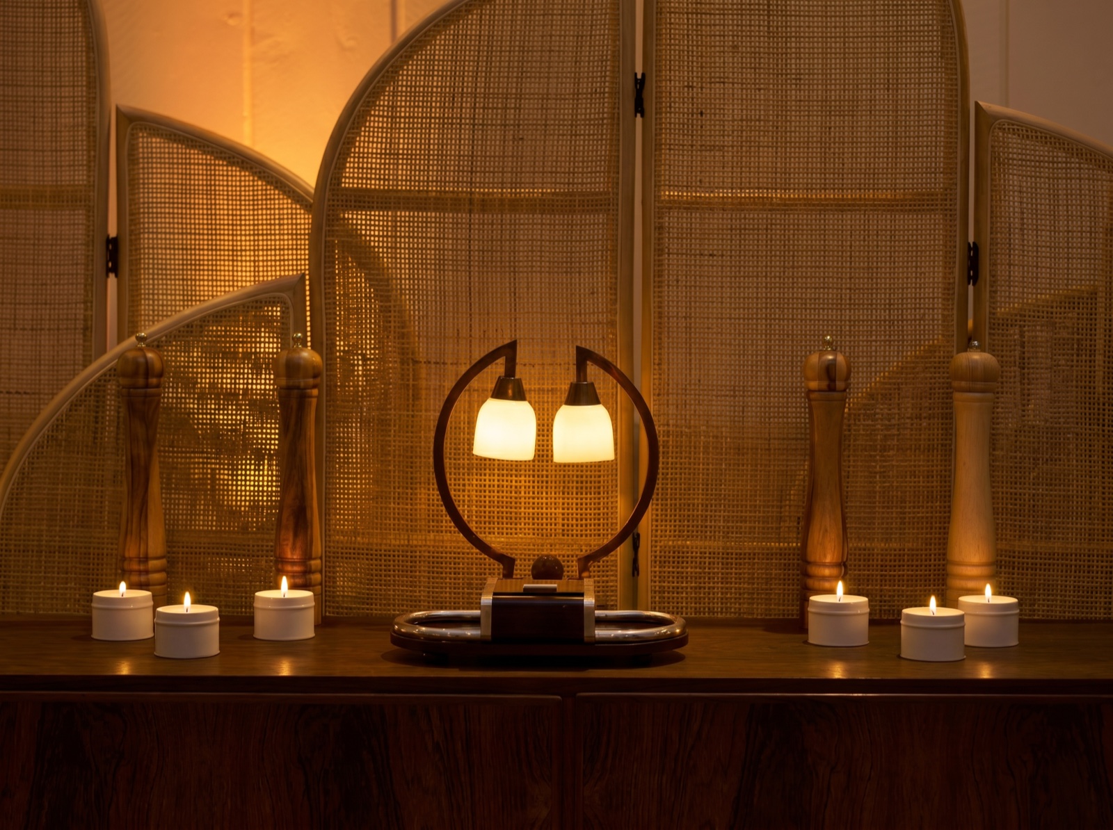 Ambiance feutrée du salon : lampe chaleureuse, bougies, paravent en cannage