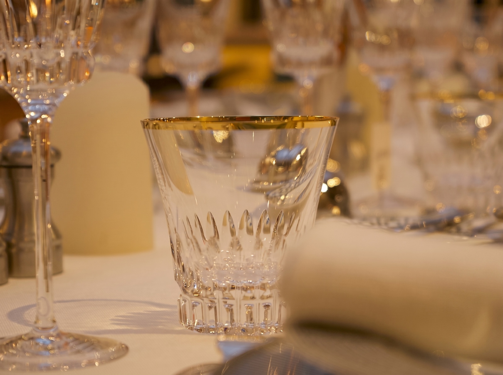 Verre en cristal taillé au liseré doré sur une table dressée, lumière de bougie